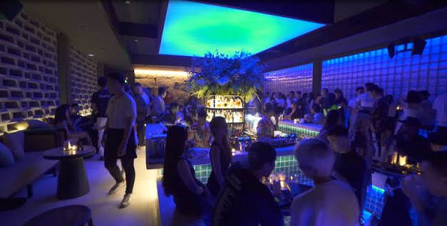 BAM BAR 蓝绿灯光时段：客人沿水池边走动，中央吧台与酒架被蓝光包围
