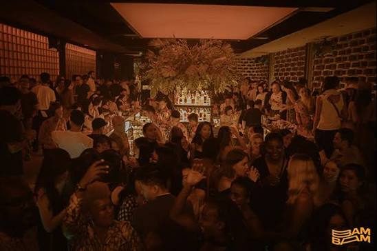 BAM BAR 暖琥珀灯光的爆满夜场：干花装置悬在中央酒架上方，全场人挤人