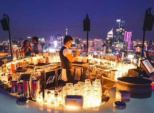 CHILL SKY BAR 中央环形吧台夜景，吧台上一整排蜡烛与玻璃杯，调酒师在圈内出品，背后是西贡高楼灯光