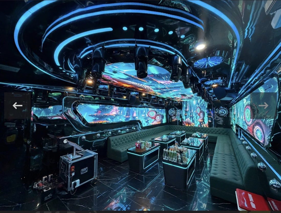 DRAGON PALACE KTV 大包厢天花同心圆蓝色光环与一排摇头灯，L 形墨绿卡座围成大圈，角落放灯光控台机箱