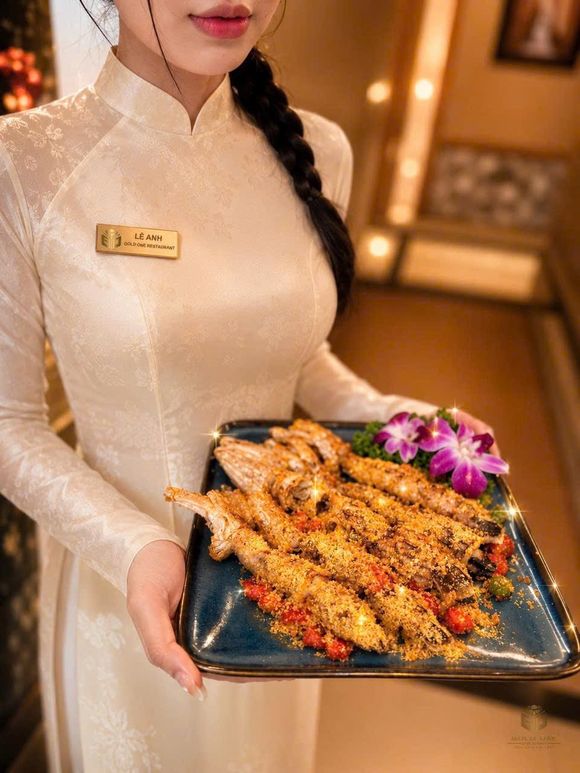 GOLD ONE 餐厅服务人员身着白色奥黛制服、佩戴餐厅金色名牌，端上一盘蒜香大头虾